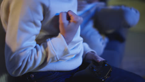 Close-Up-Of-Young-Boy-At-Home-Celebrating-Playing-With-Computer-Games-Console-On-TV-Holding-Controllers-Late-At-Night